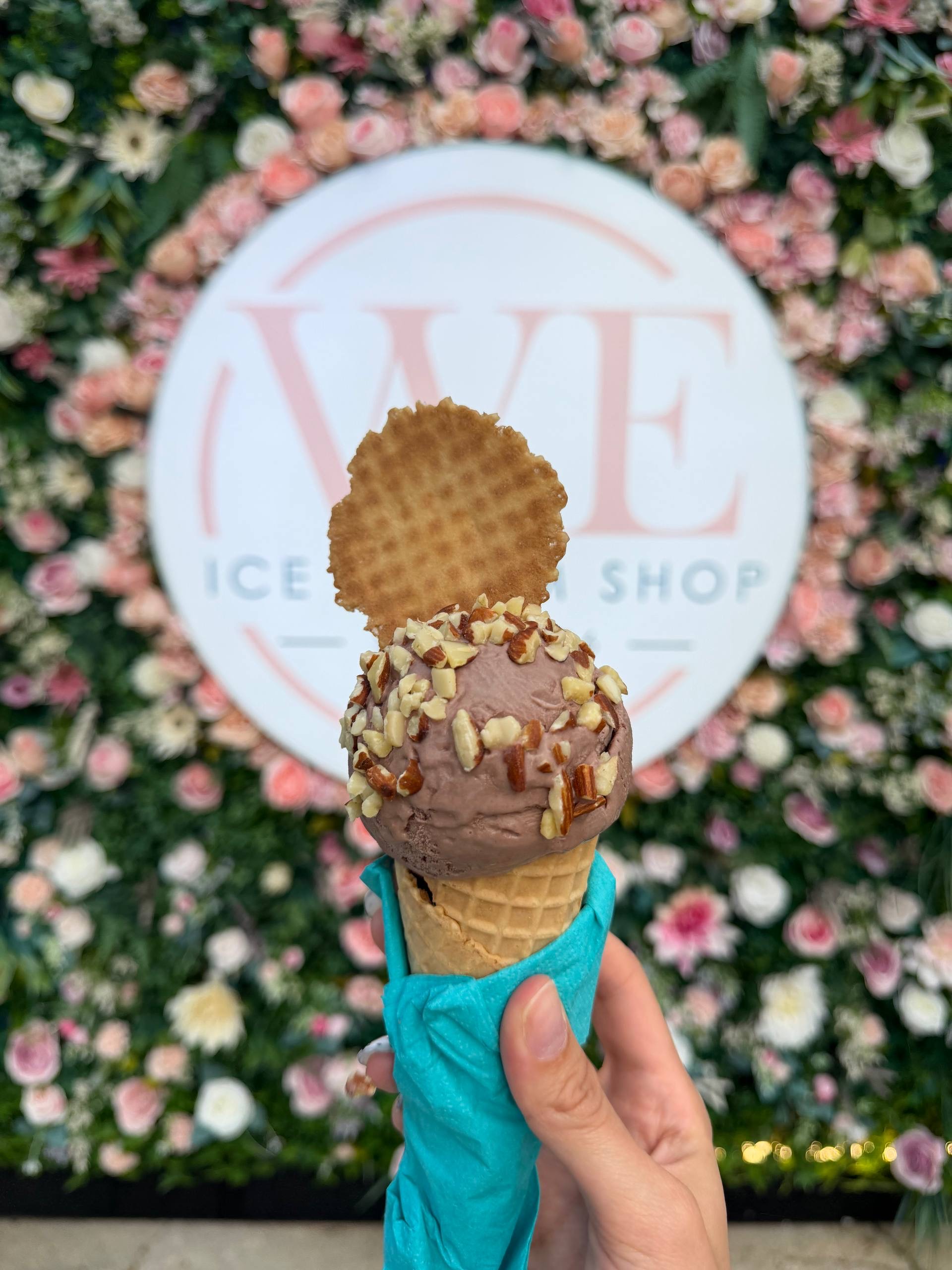 Cono de mantecado de chocolate con almendras frente al mural de flores de WE Ice Cream Shop